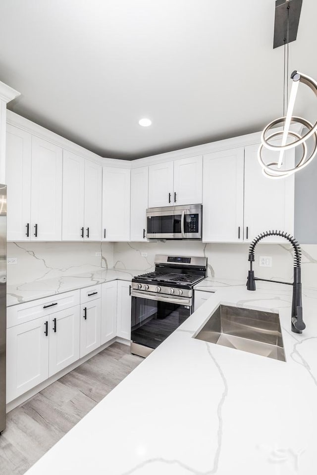 kitchen featuring light wood finished floors, appliances with stainless steel finishes, white cabinetry, and a sink