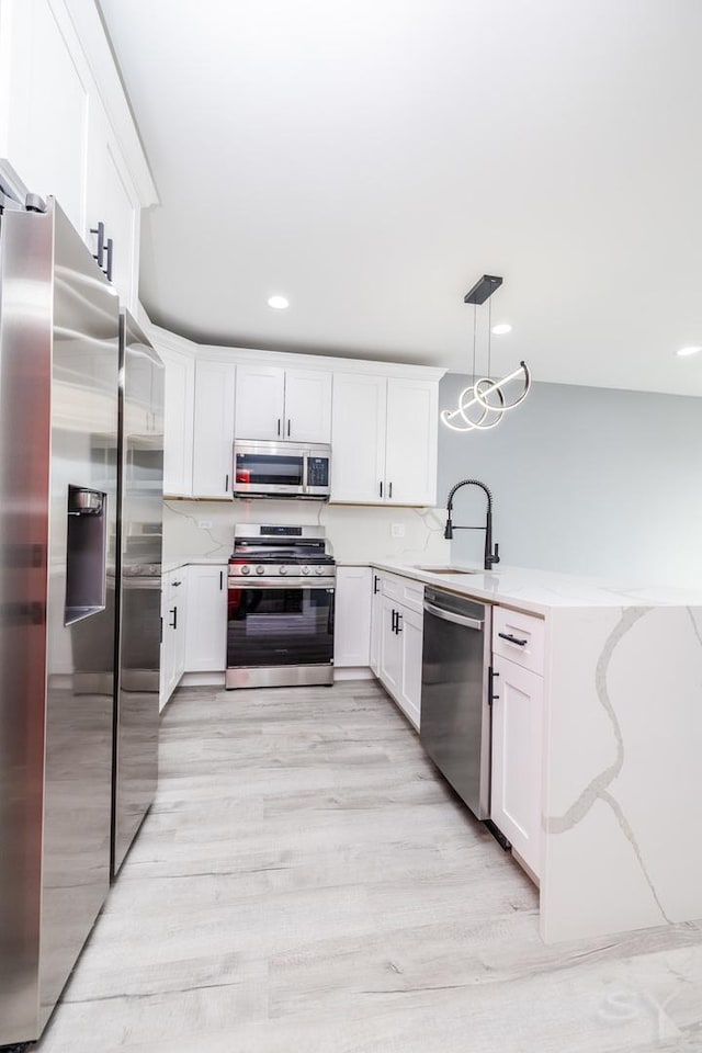 kitchen with light wood-type flooring, a peninsula, white cabinets, stainless steel appliances, and a sink