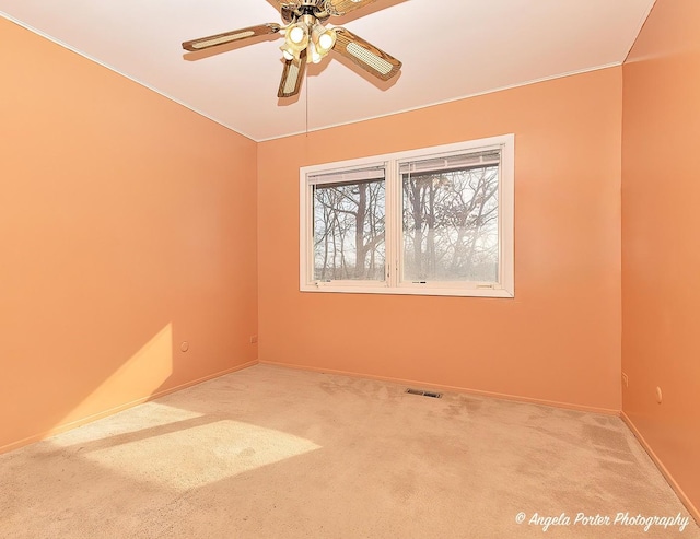 carpeted spare room with visible vents, baseboards, and a ceiling fan