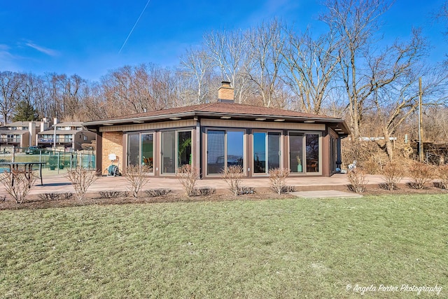 rear view of property featuring brick siding, a patio, a chimney, and a yard