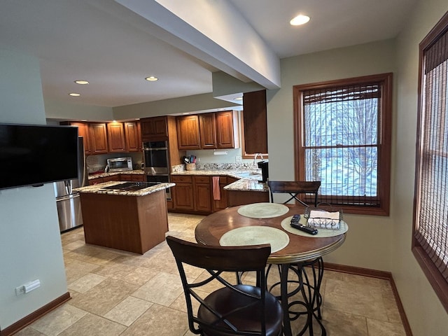 kitchen featuring a sink, a kitchen island, stainless steel double oven, baseboards, and light stone countertops