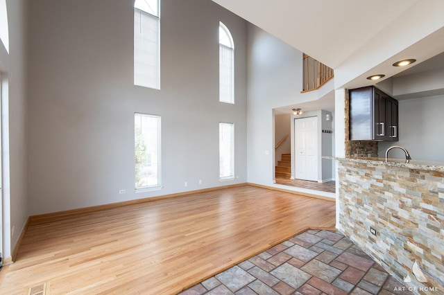 unfurnished living room featuring visible vents, baseboards, light wood finished floors, stairs, and a towering ceiling