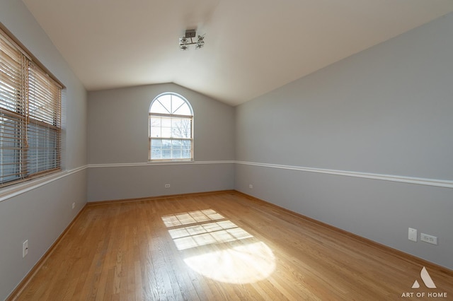 empty room featuring baseboards, lofted ceiling, and light wood-style floors