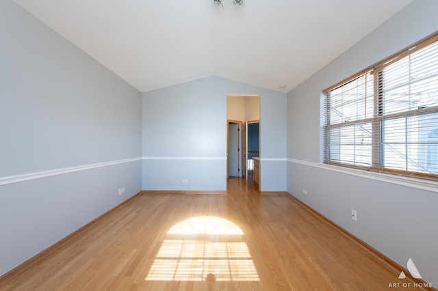 spare room featuring lofted ceiling, baseboards, and light wood finished floors