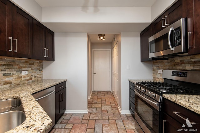 kitchen with stone tile floors, dark brown cabinets, stainless steel appliances, and baseboards