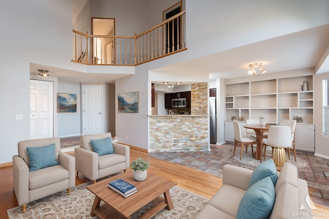 living area featuring light wood-type flooring, baseboards, and a towering ceiling