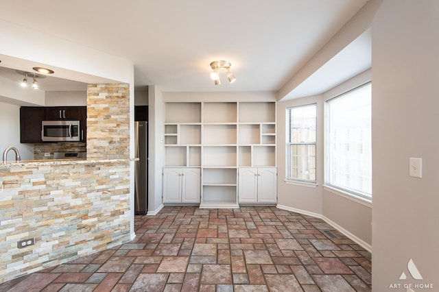 interior space featuring stainless steel appliances, dark brown cabinetry, light countertops, brick floor, and baseboards