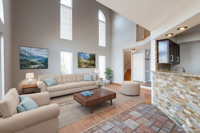 living room featuring light wood-style flooring, a high ceiling, stairs, and baseboards