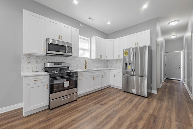 kitchen with dark wood finished floors, white cabinetry, appliances with stainless steel finishes, light countertops, and decorative backsplash