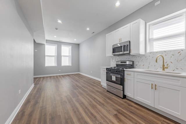 kitchen featuring dark wood-type flooring, a sink, backsplash, white cabinetry, and appliances with stainless steel finishes