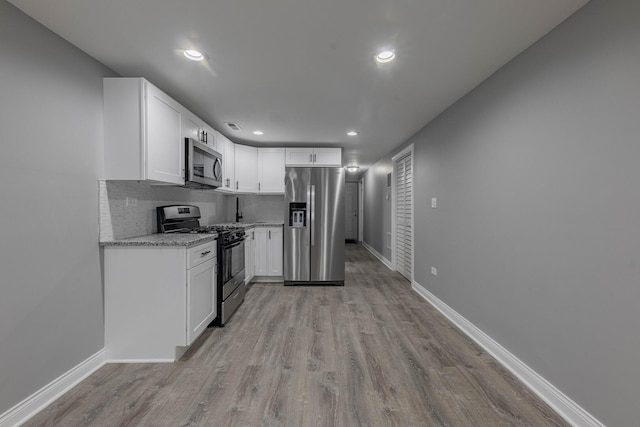 kitchen featuring baseboards, light wood-style flooring, stainless steel appliances, decorative backsplash, and white cabinetry