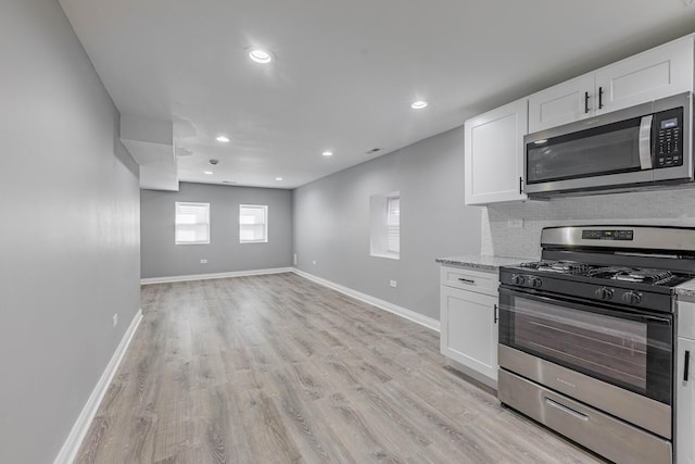 kitchen with baseboards, light wood-style flooring, stainless steel appliances, white cabinets, and backsplash