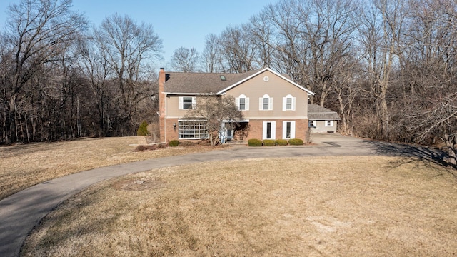 view of front facade with a front yard, brick siding, driveway, and a chimney