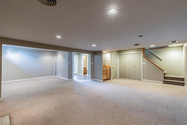 finished below grade area featuring light carpet, visible vents, stairs, and baseboards