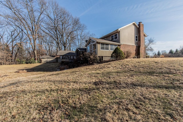 view of side of property featuring board and batten siding, a chimney, a yard, and a sunroom