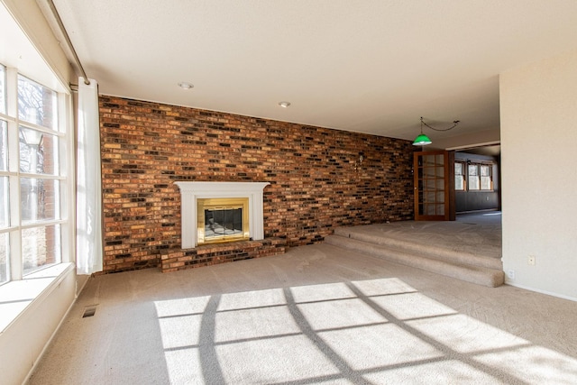 unfurnished living room featuring carpet flooring, a fireplace, brick wall, and visible vents