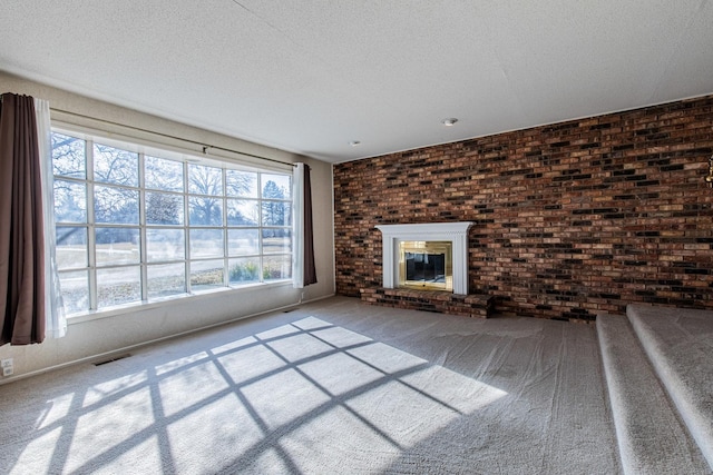 unfurnished living room with a brick fireplace, visible vents, carpet floors, and a textured ceiling