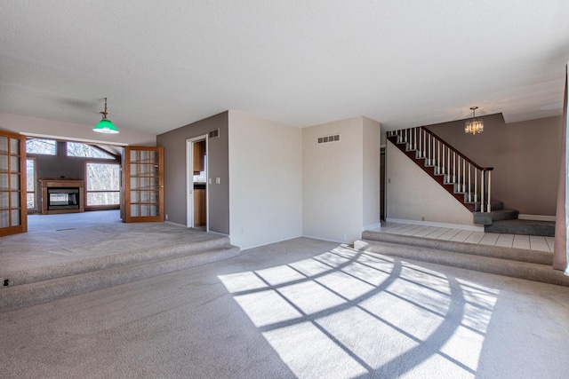 unfurnished living room with visible vents, stairs, carpet flooring, an inviting chandelier, and a glass covered fireplace