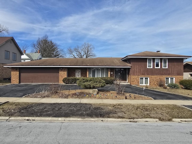 tri-level home featuring brick siding, an attached garage, and driveway