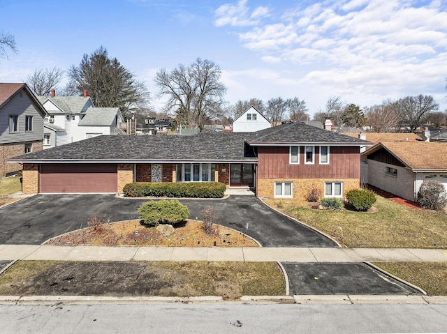 split level home featuring a front lawn, aphalt driveway, a shingled roof, a garage, and brick siding