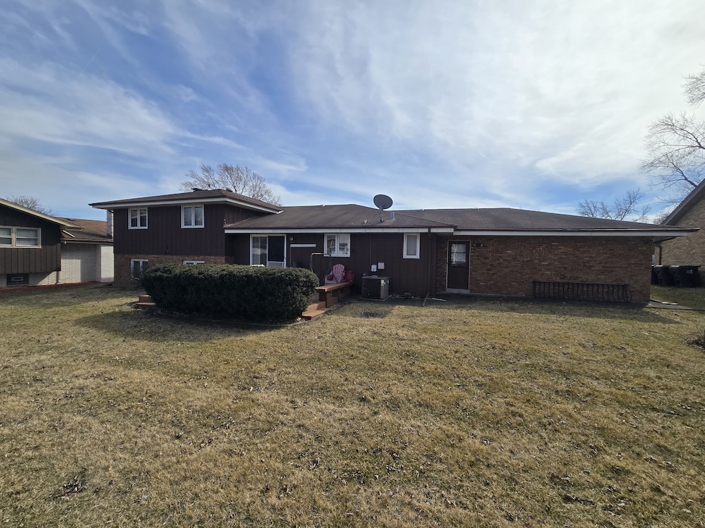 back of property with cooling unit, brick siding, and a yard