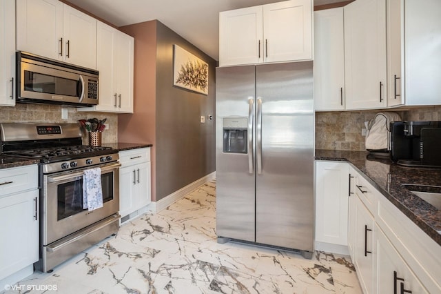 kitchen featuring baseboards, dark stone counters, stainless steel appliances, white cabinetry, and marble finish floor