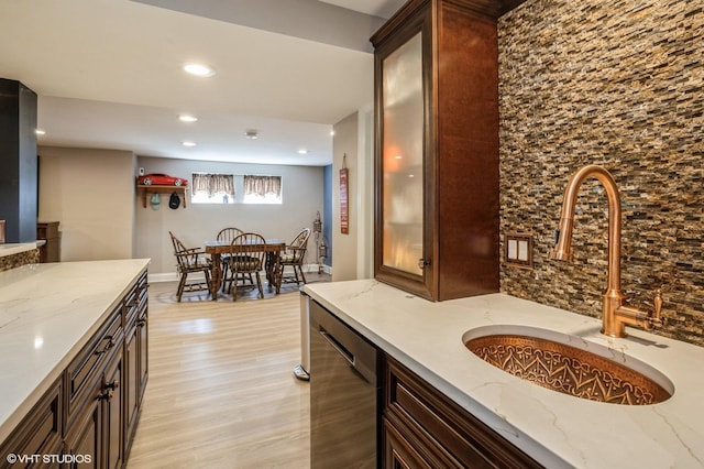 kitchen with a sink, light stone countertops, stainless steel dishwasher, and light wood-style flooring