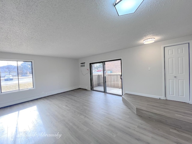 spare room featuring an AC wall unit, wood finished floors, baseboards, and a textured ceiling