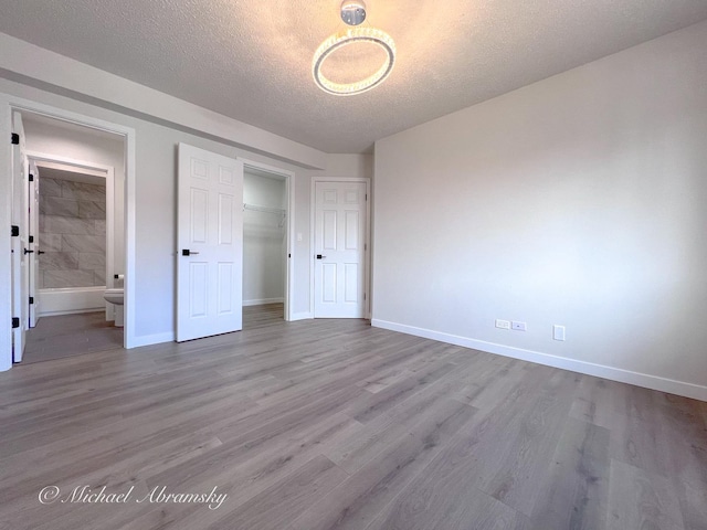 unfurnished bedroom featuring wood finished floors, baseboards, a closet, ensuite bathroom, and a textured ceiling