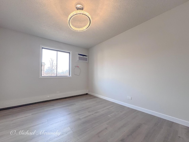 spare room with baseboard heating, an AC wall unit, baseboards, and wood finished floors