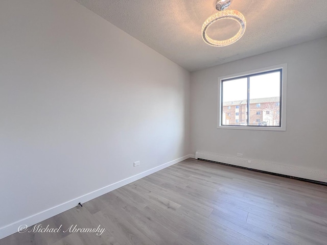 spare room featuring a baseboard radiator, baseboards, a textured ceiling, and wood finished floors