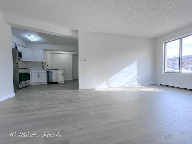 unfurnished living room with a sink, light wood-style floors, baseboard heating, and a textured ceiling