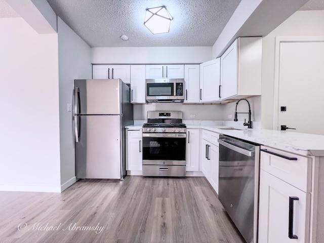 kitchen featuring light stone counters, light wood-style flooring, appliances with stainless steel finishes, white cabinets, and a sink