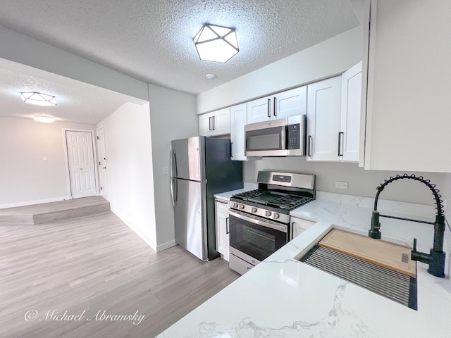 kitchen with light wood-type flooring, stainless steel appliances, a textured ceiling, white cabinetry, and a sink