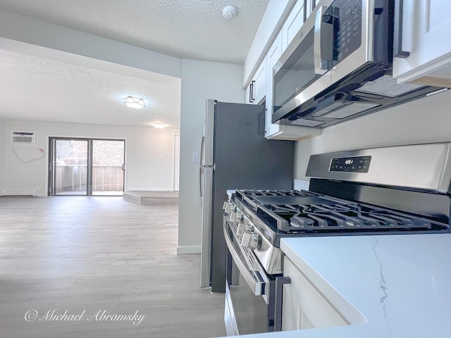 kitchen featuring baseboards, appliances with stainless steel finishes, a textured ceiling, white cabinetry, and light wood-type flooring