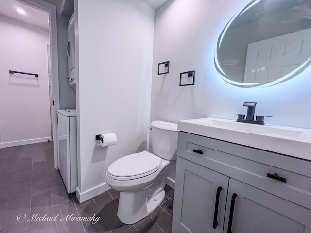 bathroom featuring vanity, stacked washer / dryer, toilet, and baseboards