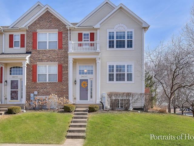 view of front of property with a front lawn, a balcony, and brick siding