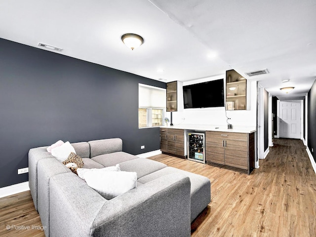 living room with wine cooler, visible vents, light wood-type flooring, and baseboards