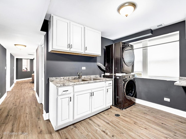 laundry area featuring cabinet space, stacked washer / dryer, light wood-style floors, and a sink