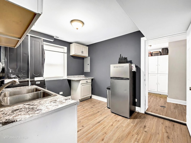 kitchen with baseboards, light wood finished floors, freestanding refrigerator, a sink, and light countertops