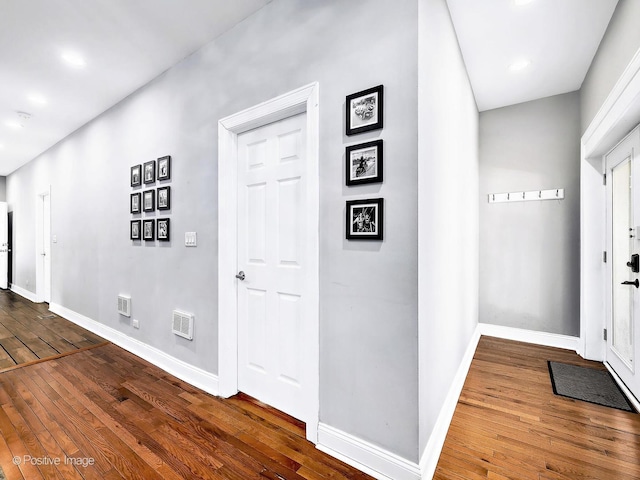 hallway featuring visible vents, dark wood-style flooring, and baseboards