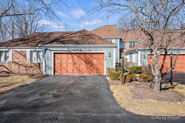 single story home featuring aphalt driveway, an attached garage, brick siding, and roof with shingles