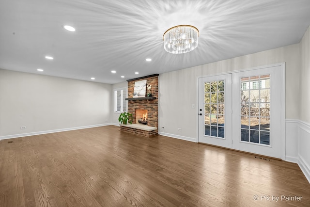 unfurnished living room featuring wood finished floors, recessed lighting, an inviting chandelier, a fireplace, and baseboards