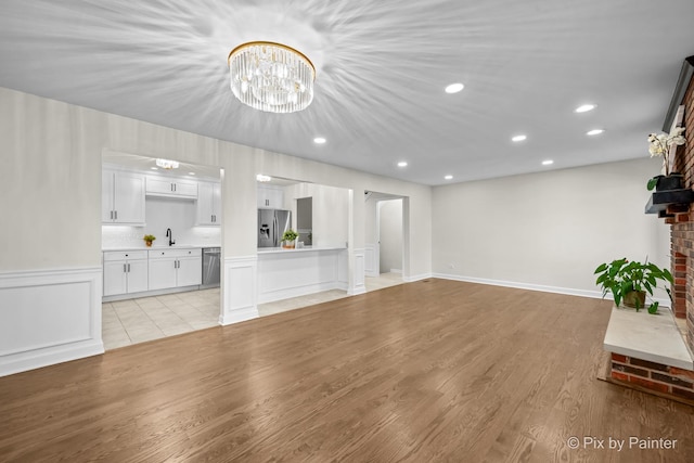 unfurnished living room featuring a chandelier, recessed lighting, light wood finished floors, and a sink