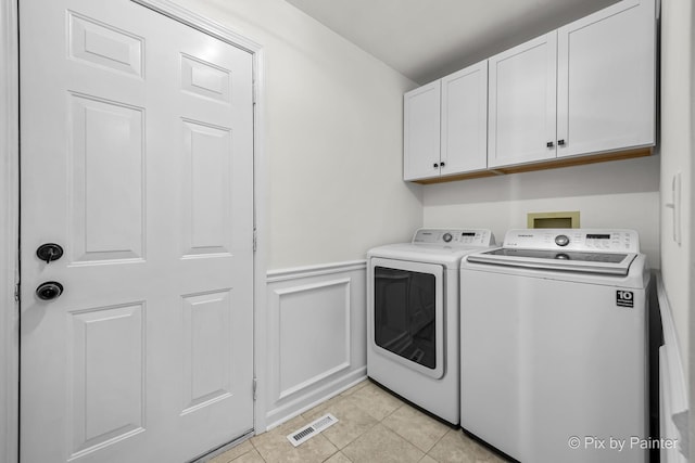 washroom with visible vents, a wainscoted wall, washer and dryer, light tile patterned flooring, and cabinet space