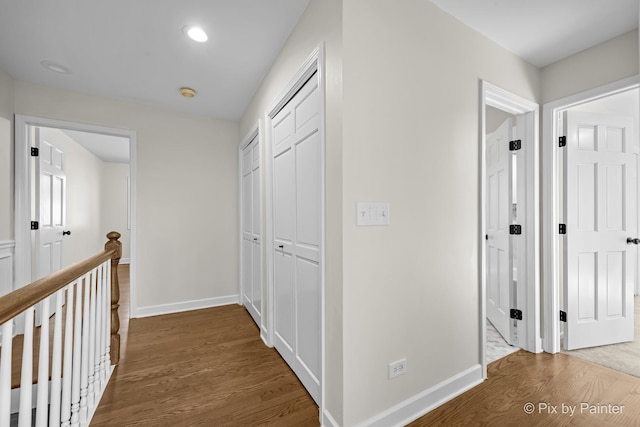 hallway with an upstairs landing, baseboards, and wood finished floors