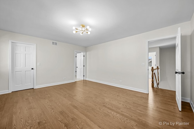 empty room featuring a notable chandelier, wood finished floors, visible vents, and baseboards