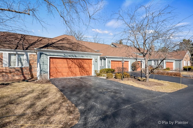 single story home featuring aphalt driveway, a garage, and brick siding