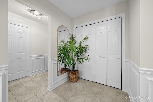 entryway featuring light tile patterned floors, wainscoting, and a decorative wall