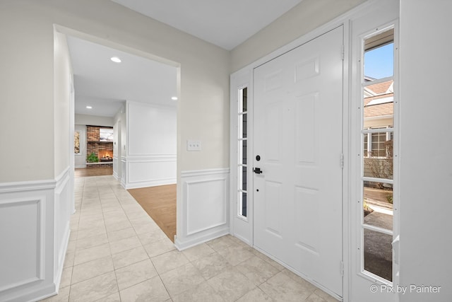 entrance foyer featuring a brick fireplace, a decorative wall, a wealth of natural light, and wainscoting